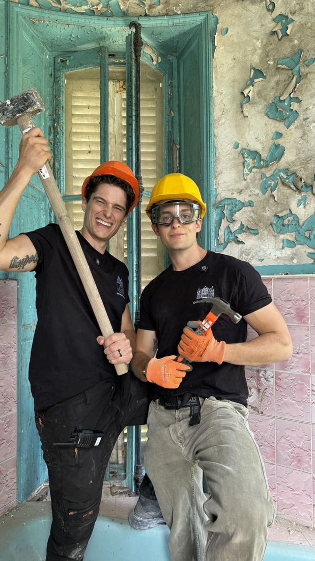 Tom and Damien in hard hats with a sledgehammer before demolition